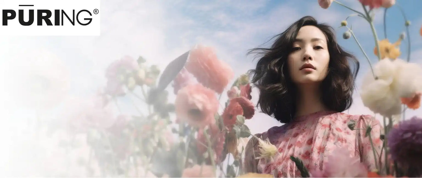 Egy nő sötét, hullámos hajjal és virágos ruhában, akit színes virágok vesznek körül, és közvetlenül a nézőre néz.