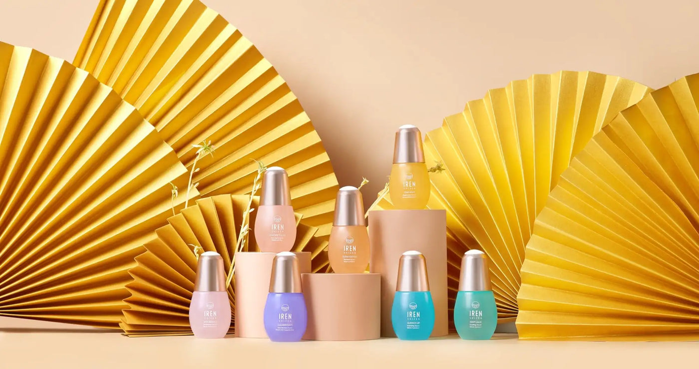 Kék és zöld üvegpalackok ezüst kupakokkal, bézs háttér előtt elrendezve.