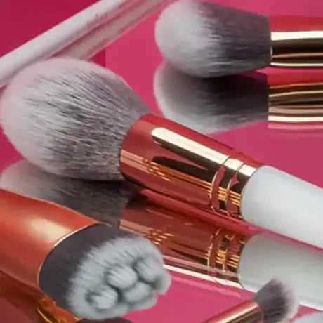 Egy gyűjtemény sminkecsetekből, fehér és szürke sörtékkel, és rózsaarany ferrulákkal.
